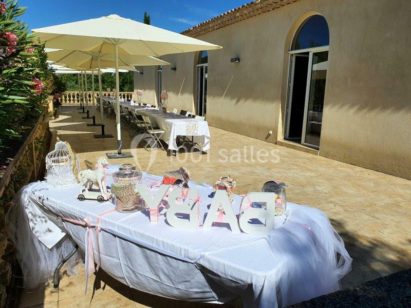 Table décorée pour une fête en plein air, avec des lettres ’BABY’ et des bonbonnières, sur une terrasse ensoleillée.