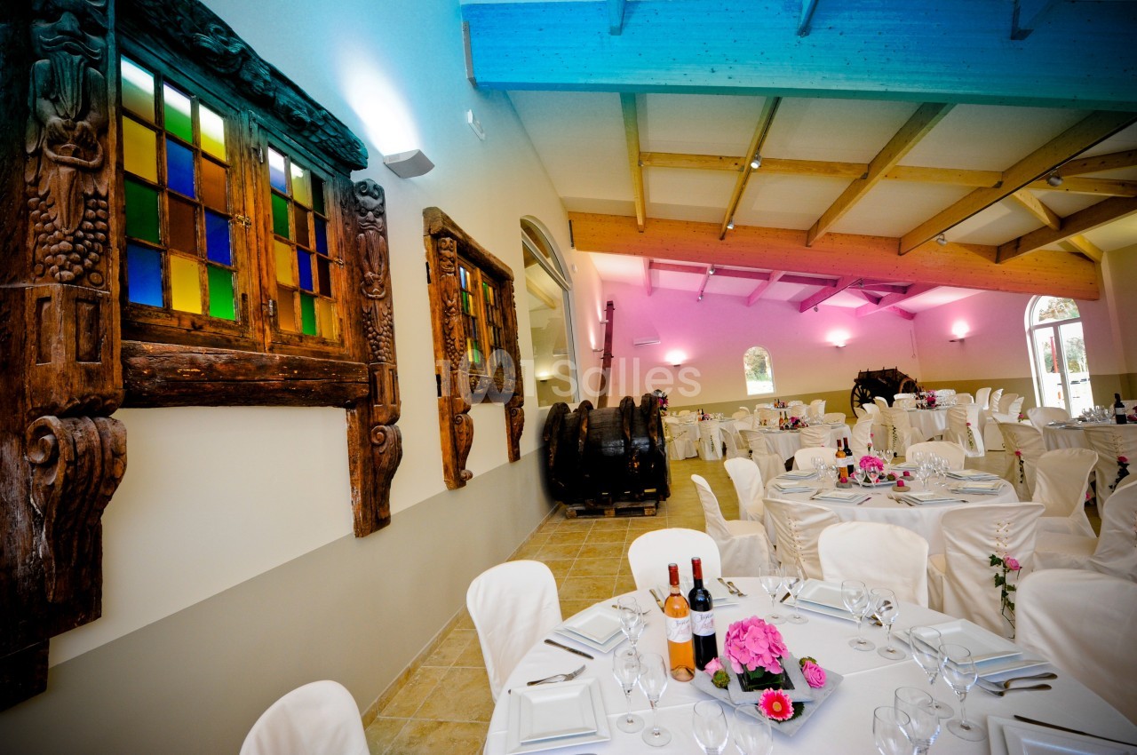 Salle de réception décorée avec des tables dressées, des fenêtres en bois sculpté et des tonneaux en arrière-plan.