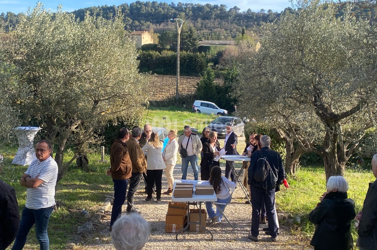 Groupe de personnes rassemblées en plein air dans un verger d'oliviers, discutant autour d'une table avec des documents.
