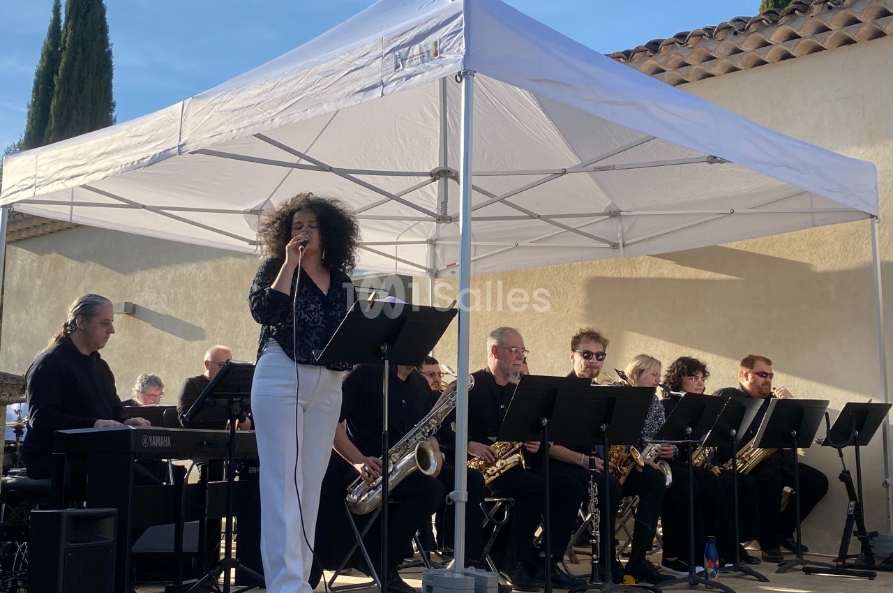 Une chanteuse interprète sur scène avec un groupe de musiciens sous une tente blanche en extérieur.