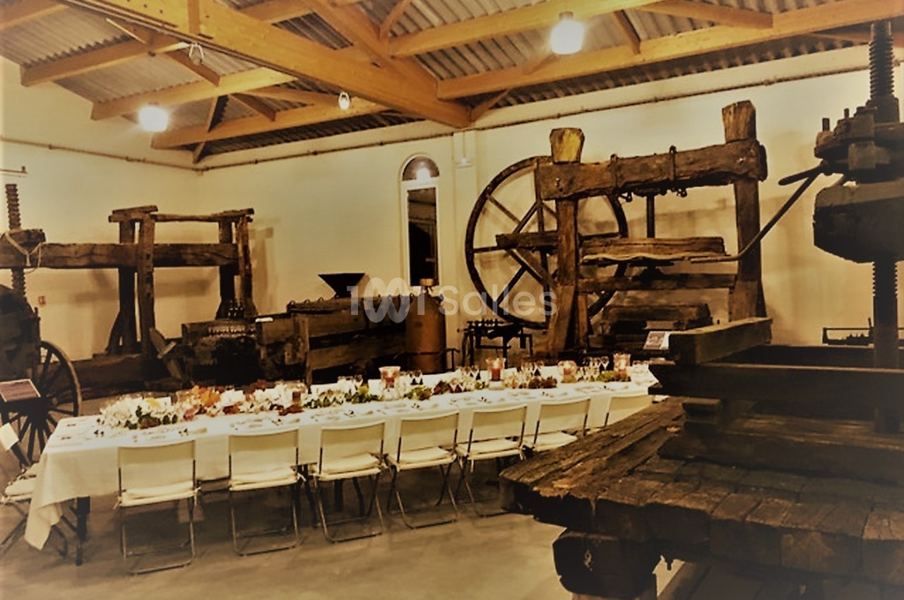 Salle avec de grandes presses anciennes en bois et une longue table dressée pour un repas.