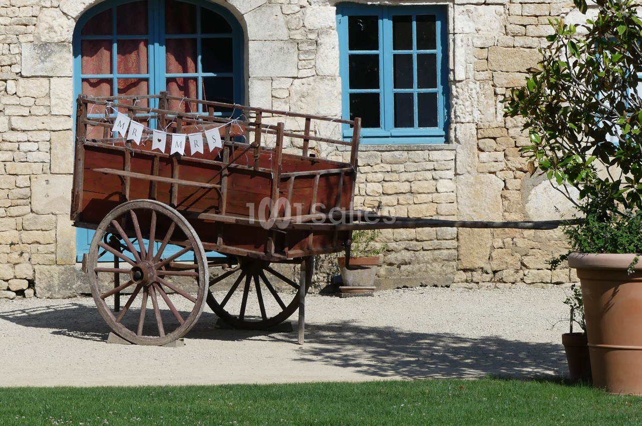 Charrette en bois ancienne avec des roues en métal, décorée d'une guirlande, devant un bâtiment en pierre.