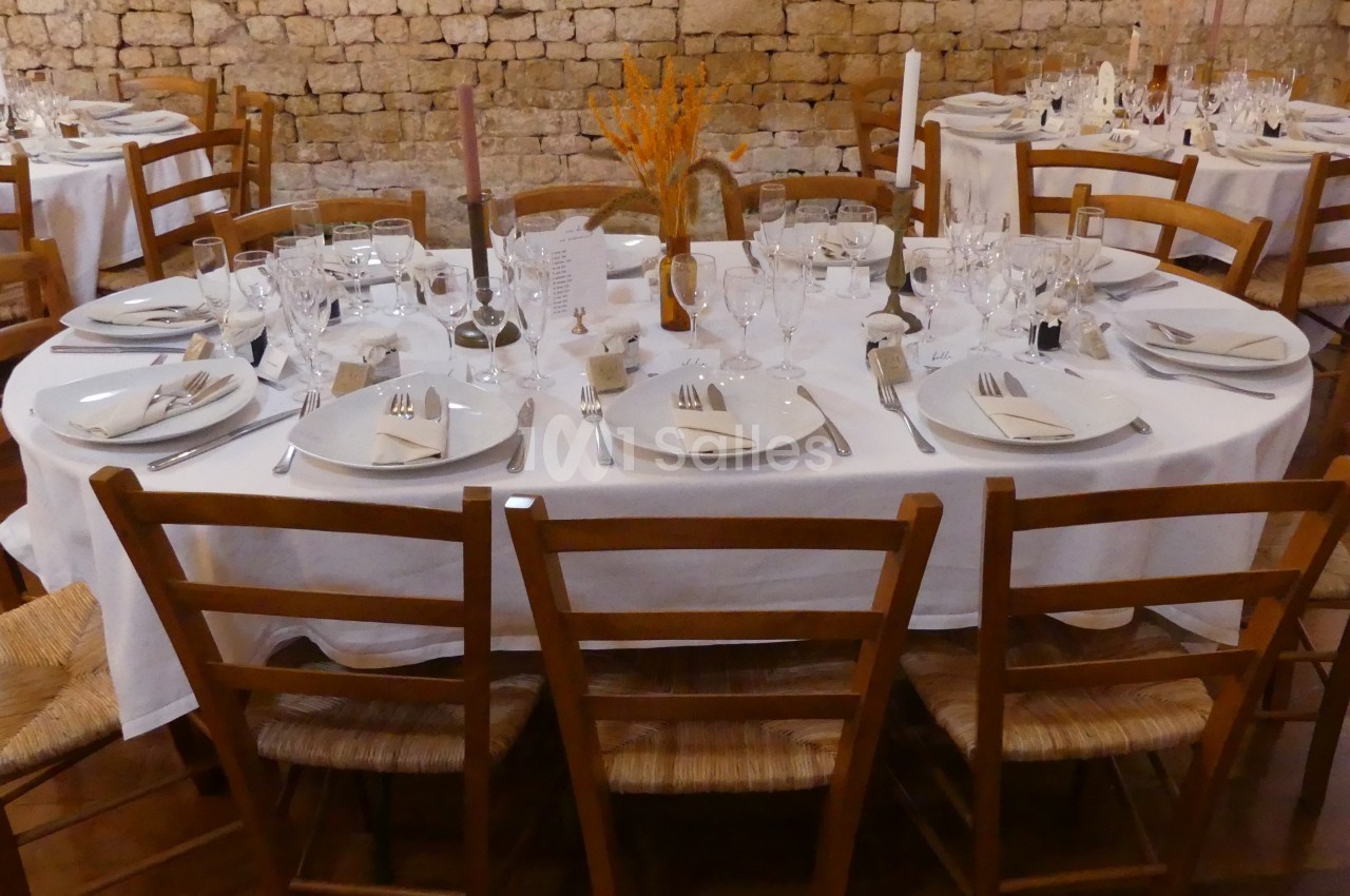 Table ronde dressée pour un repas, avec nappes blanches, vaisselle, verres et décoration florale au centre.