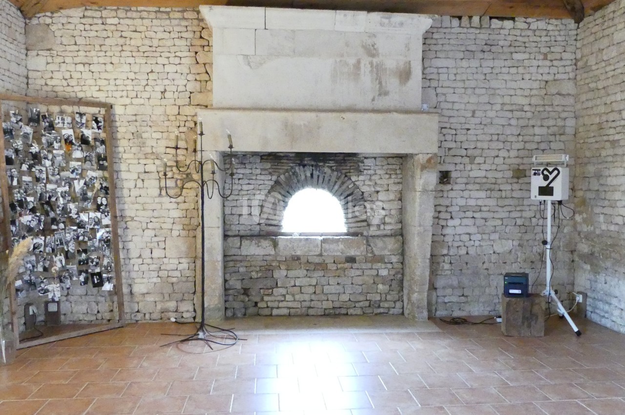 Salle en pierre avec cheminée ancienne, mur décoré de photos en noir et blanc et équipement technique à droite.