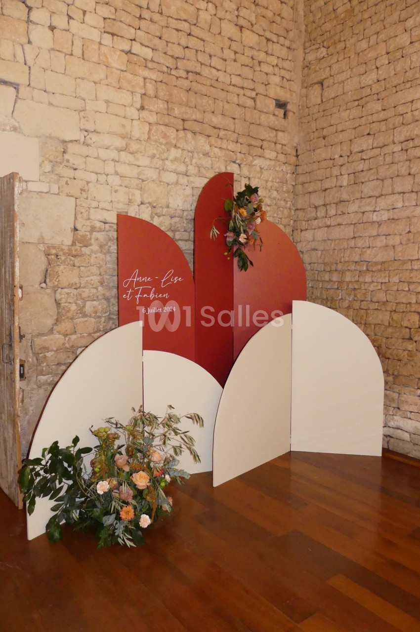 Mur décoratif en panneaux rouges et blancs avec des fleurs, installé dans une pièce aux murs en pierre.