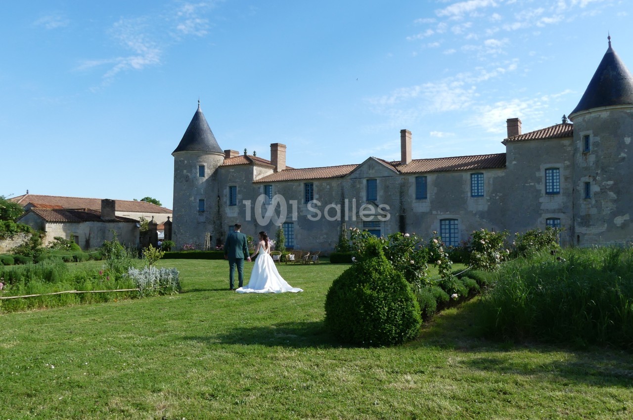 Un couple marche dans le jardin d'un château ancien entouré de verdure par une journée ensoleillée.