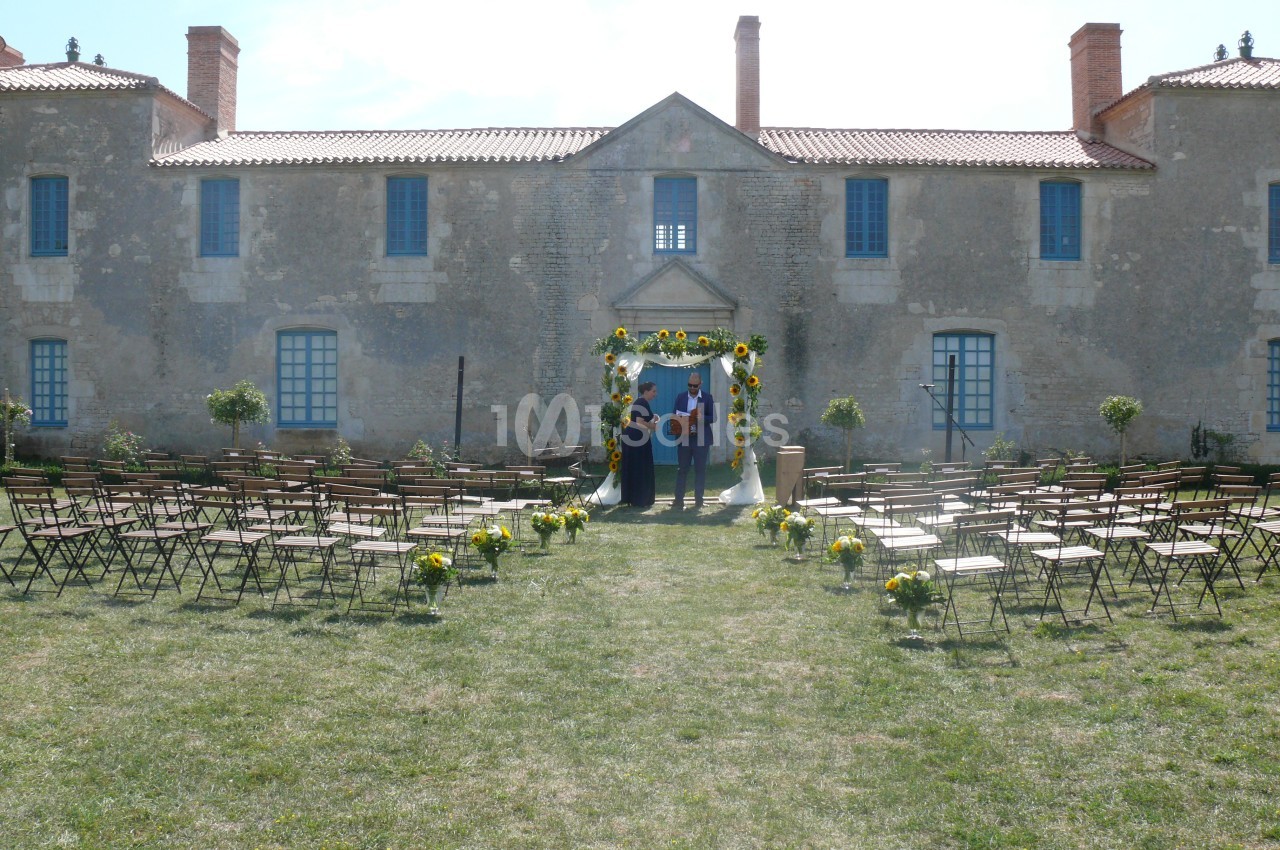 Chaises alignées en extérieur devant une arche fleurie, avec un bâtiment en pierre en arrière-plan.