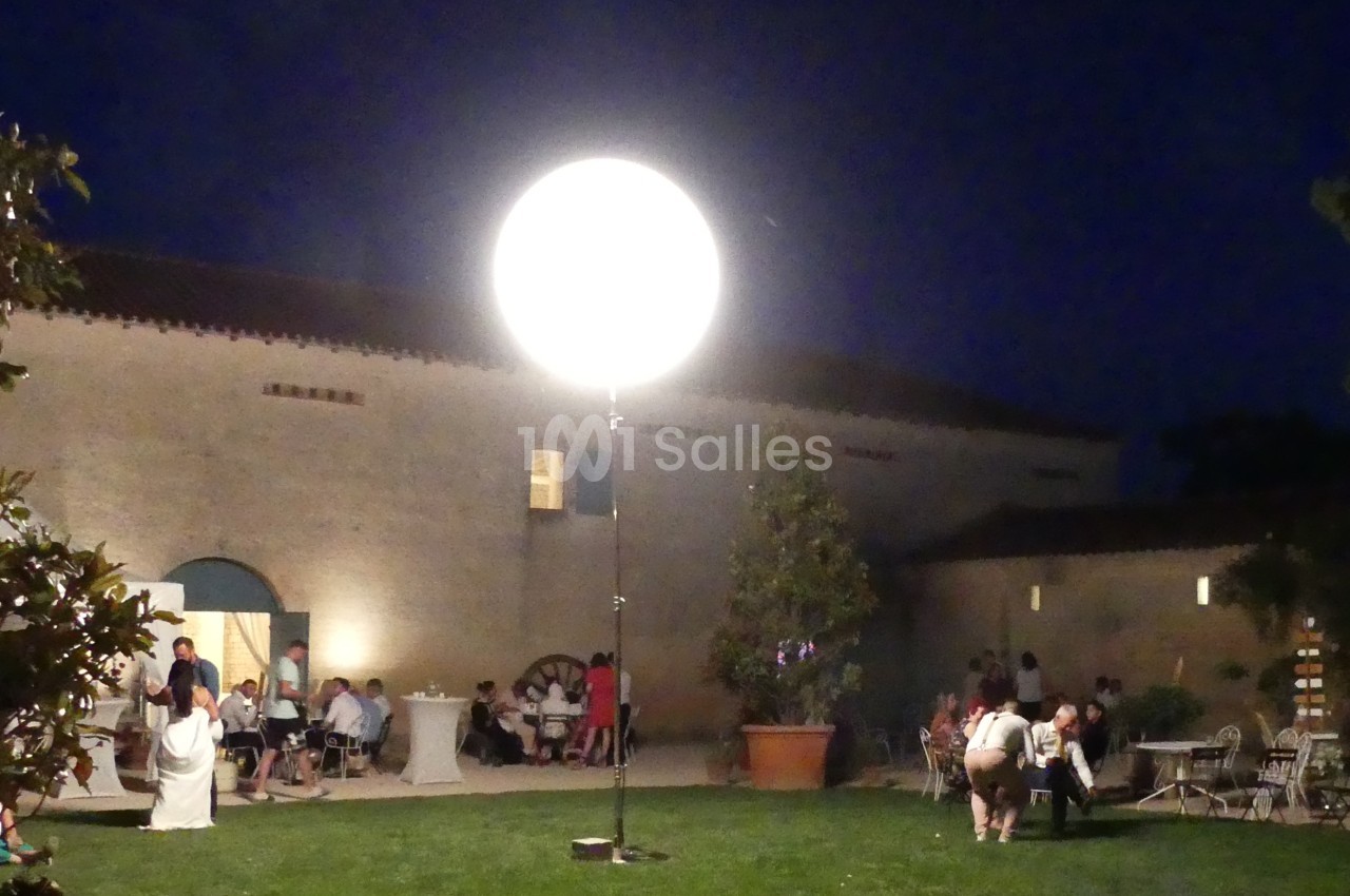 Groupe de personnes assises et debout dans une cour extérieure éclairée par une grande lampe ronde, de nuit.