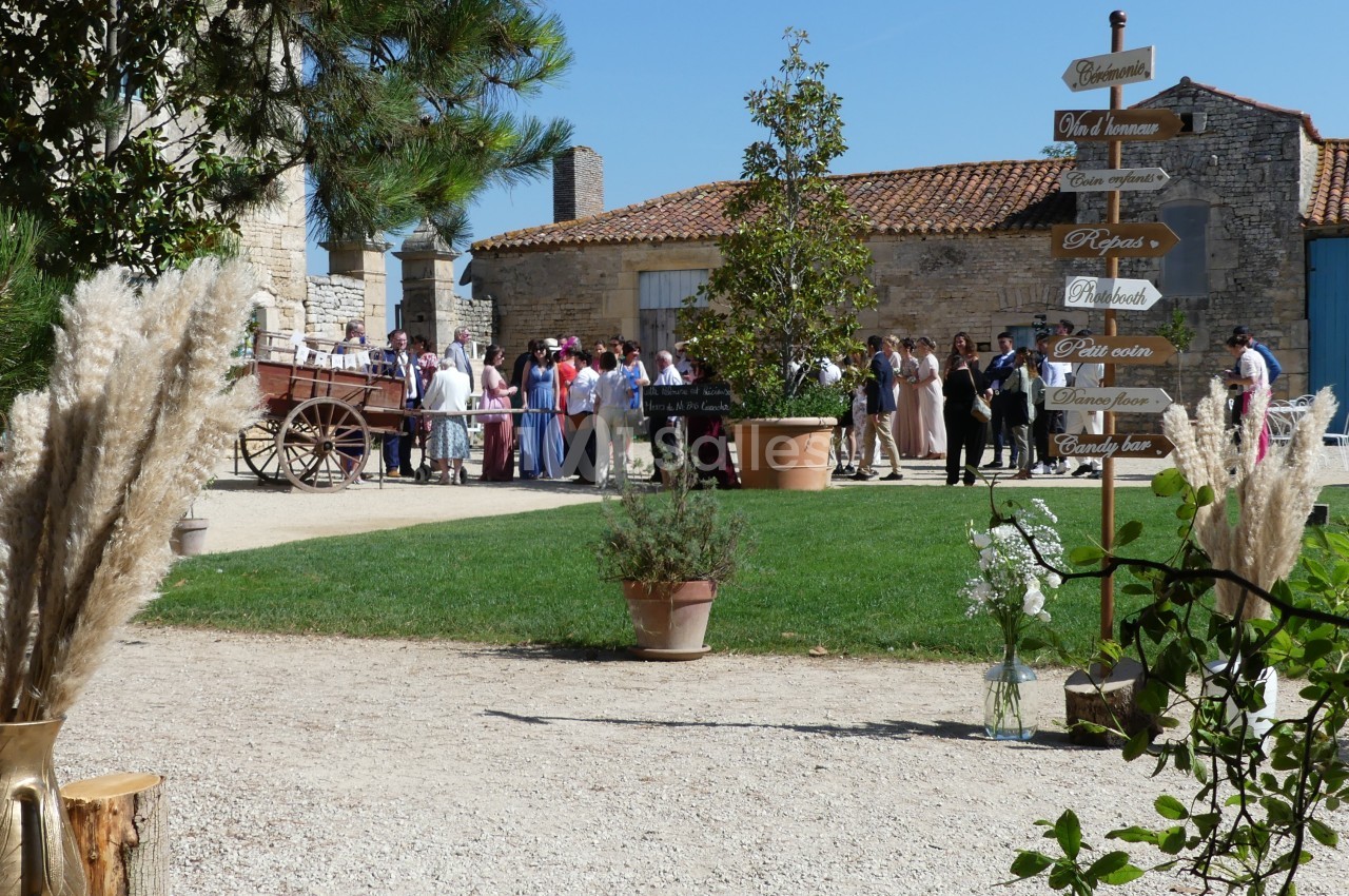 Groupe de personnes rassemblées dans une cour extérieure près d'un panneau directionnel et de décorations florales.