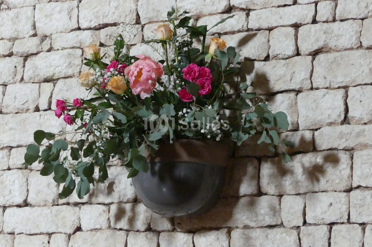 Bouquet de fleurs colorées dans un vase mural en métal, fixé sur un mur en pierre apparente.