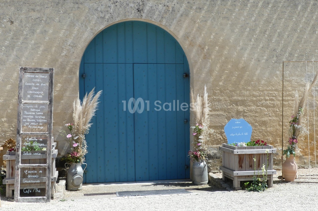 Porte bleue arrondie encadrée de décorations florales et panneaux en bois devant un mur en pierre clair.