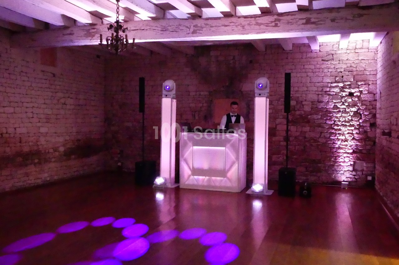 Un DJ derrière une table lumineuse dans une salle en pierre avec éclairage violet et parquet en bois.