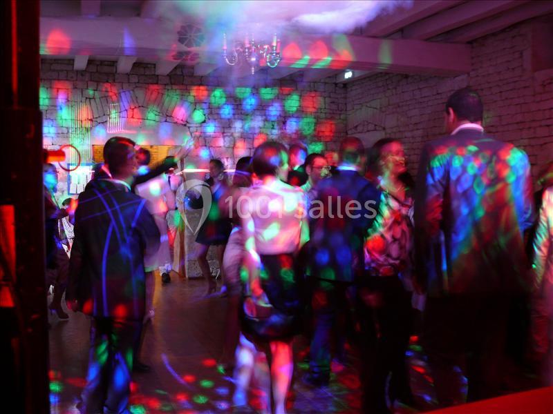 Personnes dansant sous des lumières colorées dans une salle avec murs en pierre et plafond en poutres apparentes.