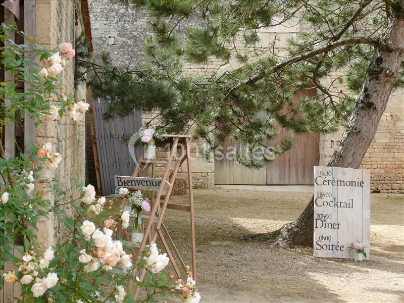 Panneaux en bois indiquant les étapes d'un événement dans une cour rustique avec des fleurs et un grand arbre.