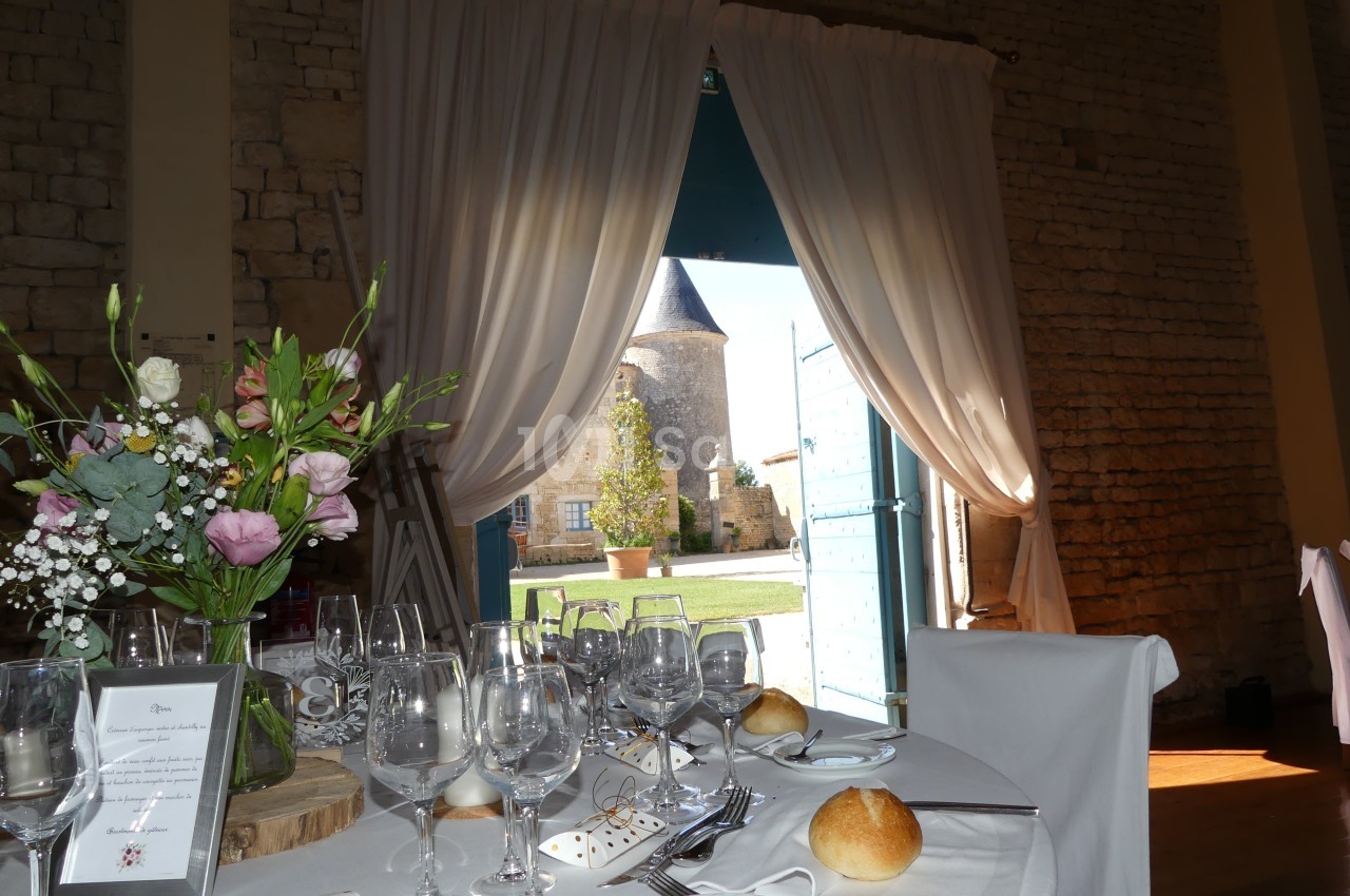 Table dressée avec vaisselle élégante, fleurs et vue sur une cour extérieure avec une tour en arrière-plan.