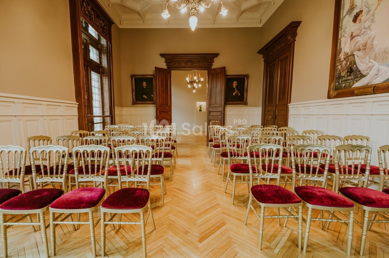Rangées de chaises dorées avec assises rouges disposées dans une salle élégante au parquet clair et murs ornés.