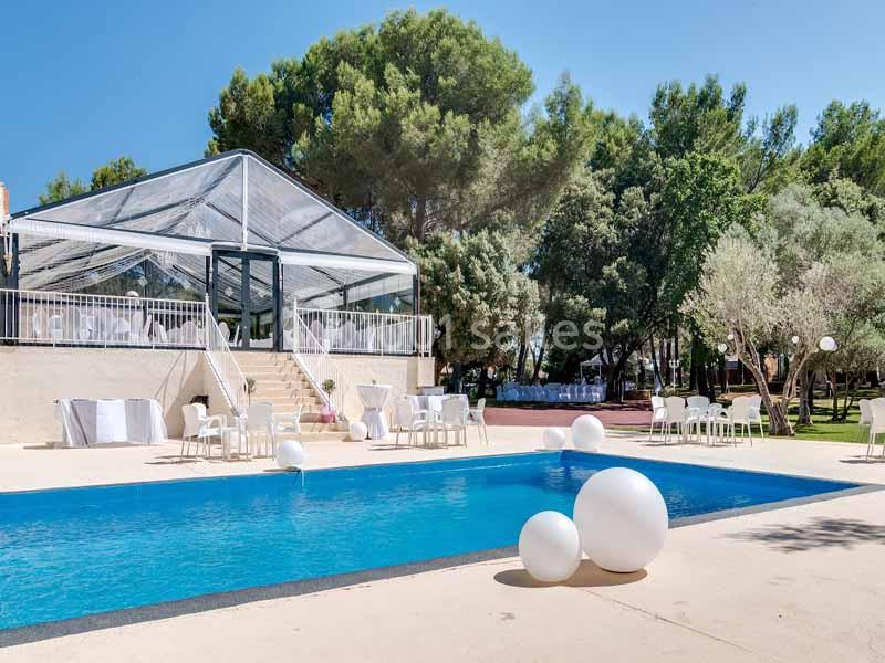 Piscine extérieure avec des décorations blanches, entourée d'arbres et d'une structure transparente en arrière-plan.