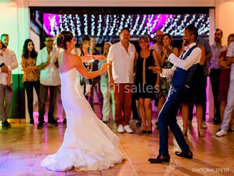 Un couple danse lors d'une réception de mariage, entouré d'invités et d'une décoration lumineuse.