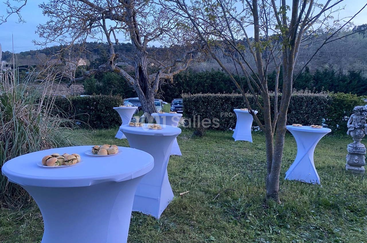 Tables hautes blanches dressées avec des plateaux de sandwichs dans un jardin au crépuscule.