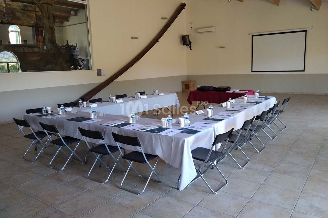Salle de réunion avec deux rangées de tables dressées, chaises pliantes, écran de projection et matériel de présentation.