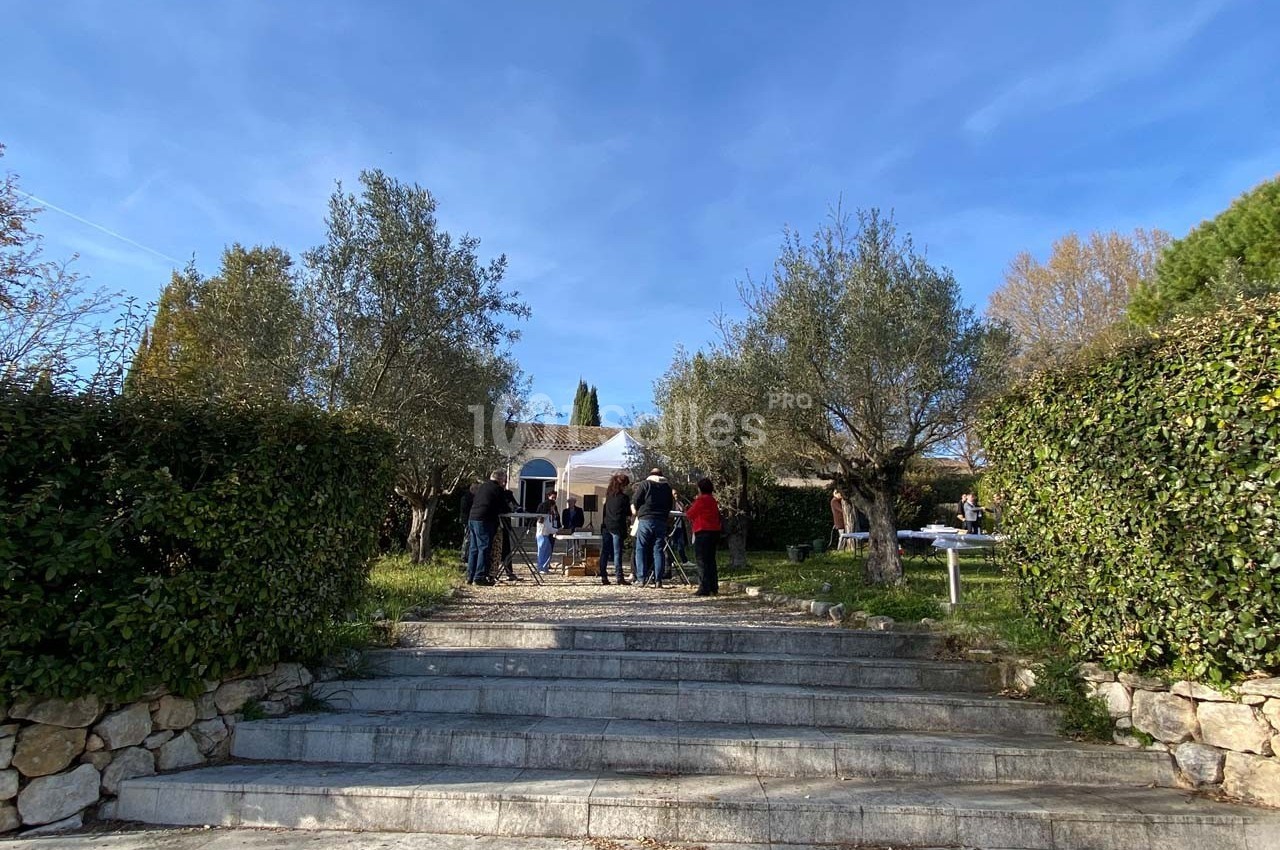 Groupe de personnes rassemblées dans un jardin devant une maison blanche entourée d'arbres et de haies.