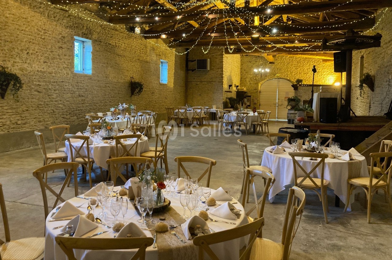Salle de réception en pierre avec tables rondes dressées, décorations lumineuses suspendues et ambiance chaleureuse.