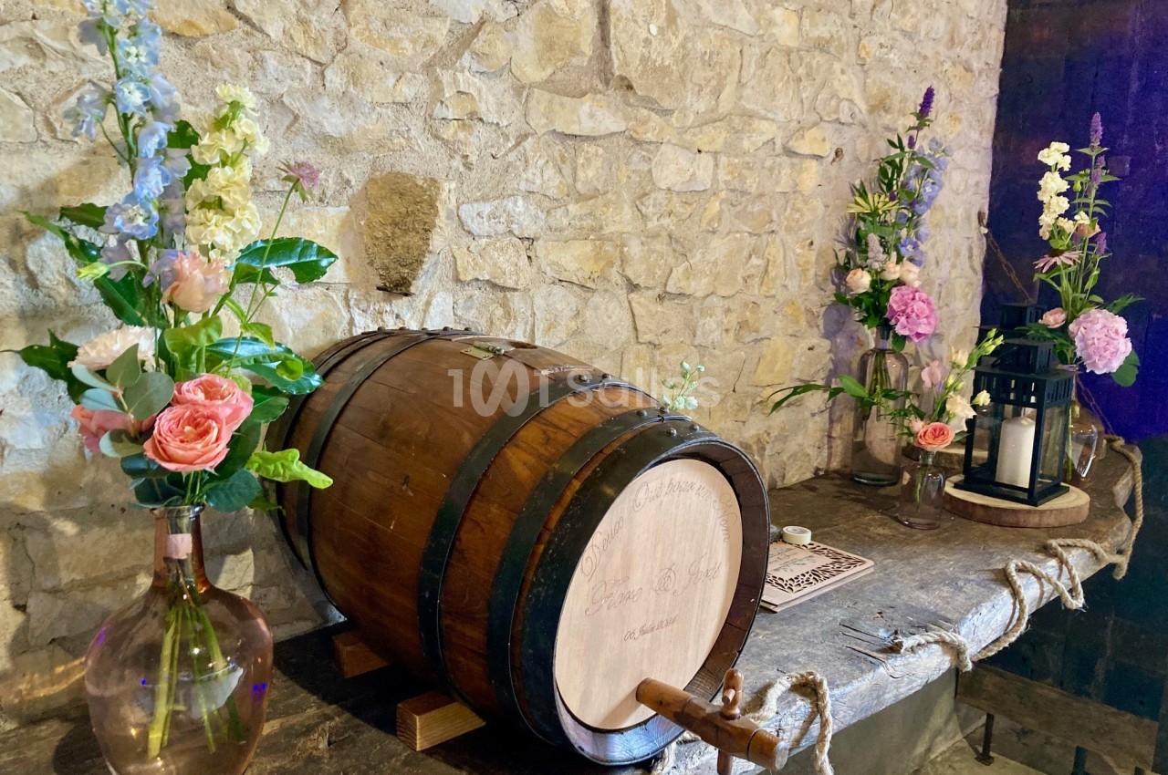 Baril en bois sur une table en pierre, entouré de fleurs colorées et de lanternes dans un décor rustique.