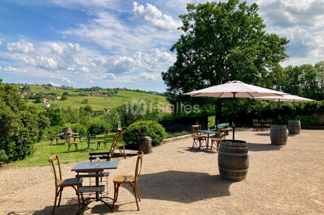 Terrasse extérieure avec tables, chaises et parasols, offrant une vue sur un paysage vallonné et verdoyant.