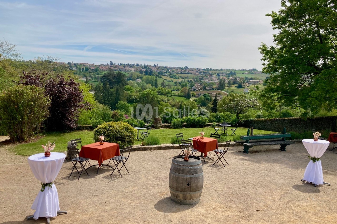 Terrasse extérieure avec tables et chaises, vue sur un paysage verdoyant et vallonné sous un ciel dégagé.