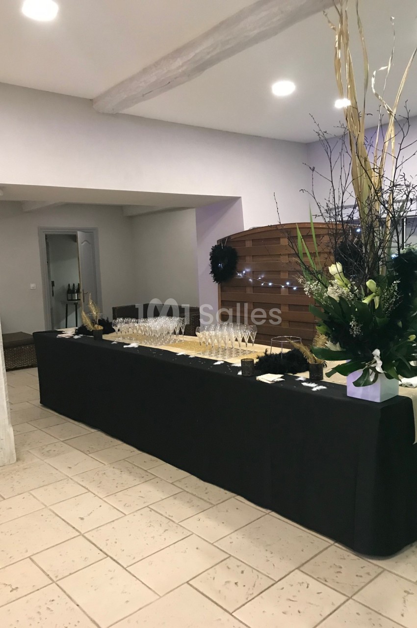 Table décorée avec une nappe noire, des verres à pied alignés et un grand bouquet floral dans une salle lumineuse.
