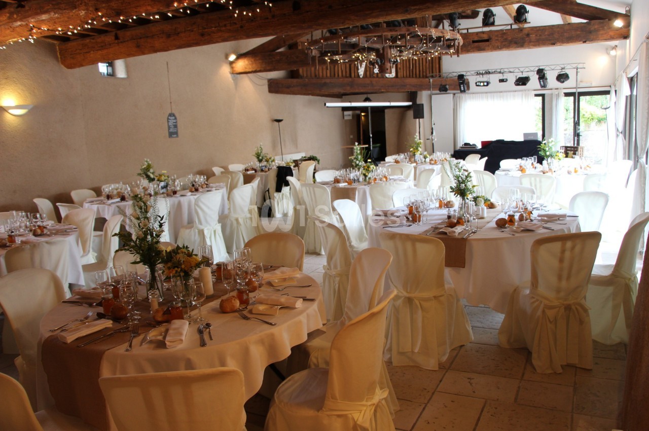 Salle de réception décorée avec des tables rondes dressées, nappes blanches et arrangements floraux.