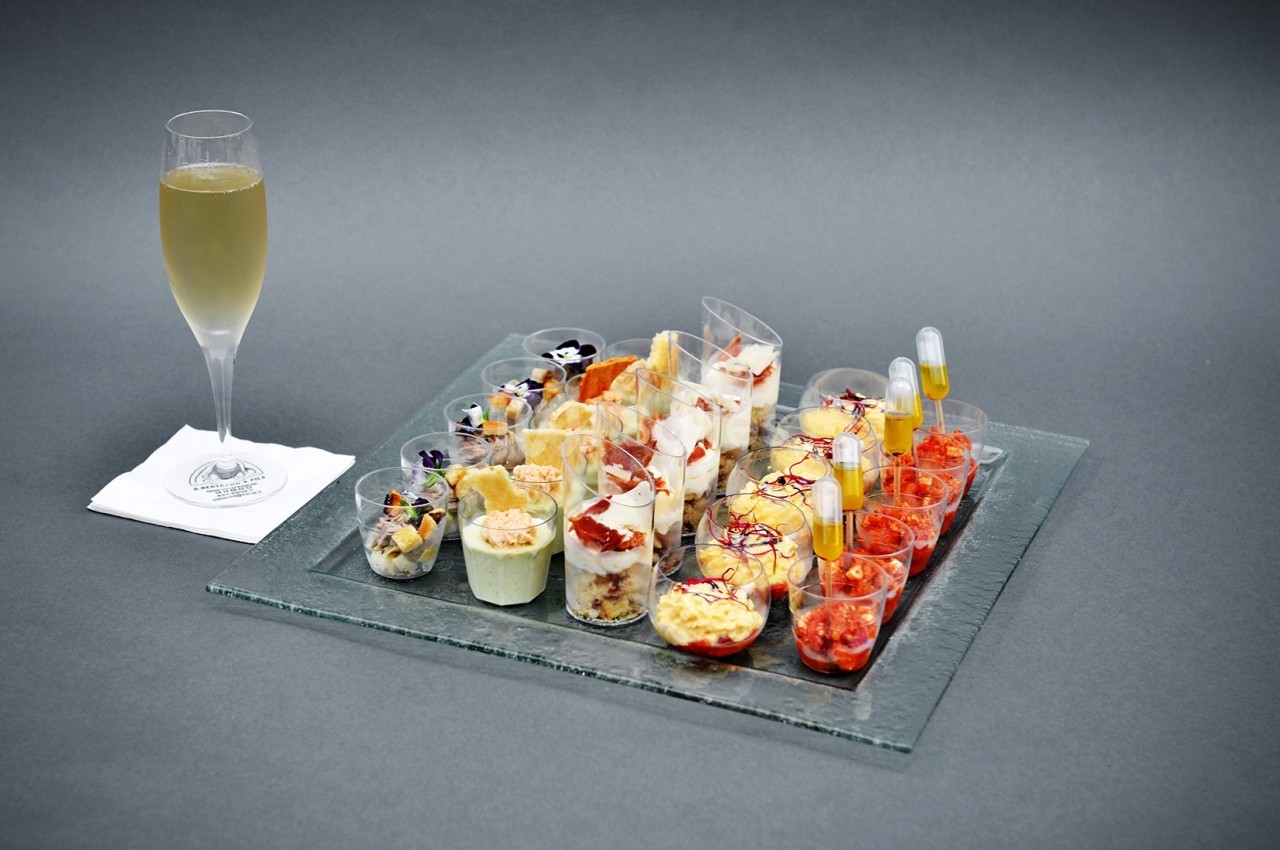 Plateau de verrines variées avec une flûte de boisson pétillante sur une serviette blanche.