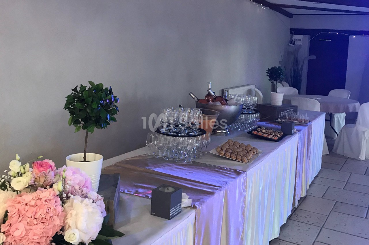 Table de réception dressée avec des fleurs, des verres, des desserts et un seau à champagne dans une salle décorée.