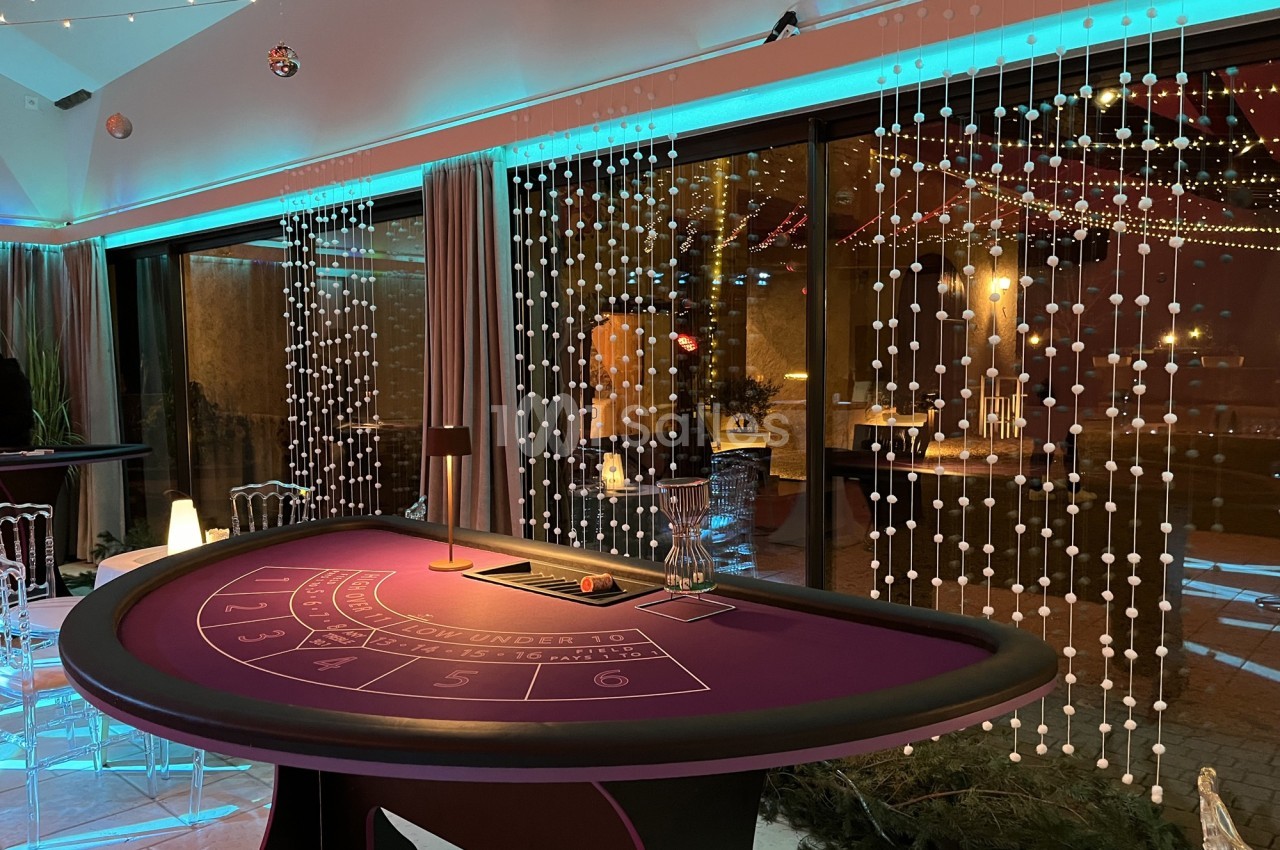 Table de jeu de casino violette dans une salle décorée avec des lumières et des guirlandes, ambiance festive.