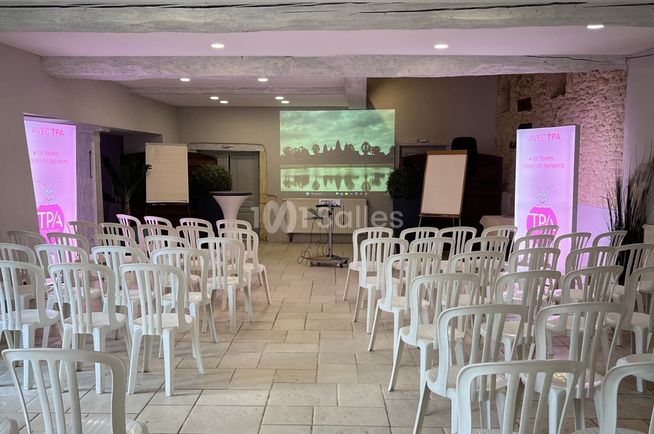 Salle de conférence avec chaises blanches alignées, projecteur affichant une image de paysage sur un écran.