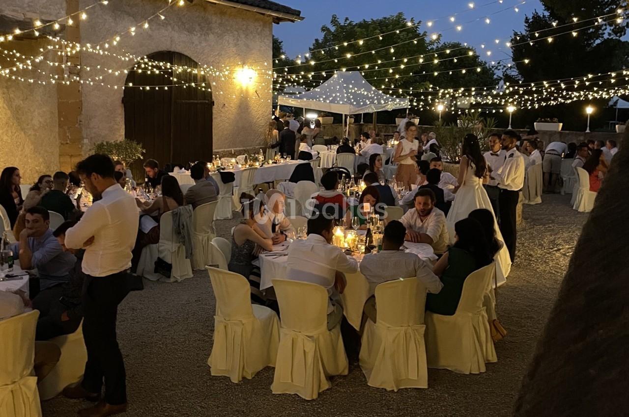 Invités dînant en soirée dans une cour éclairée par des guirlandes lumineuses, ambiance festive et conviviale.