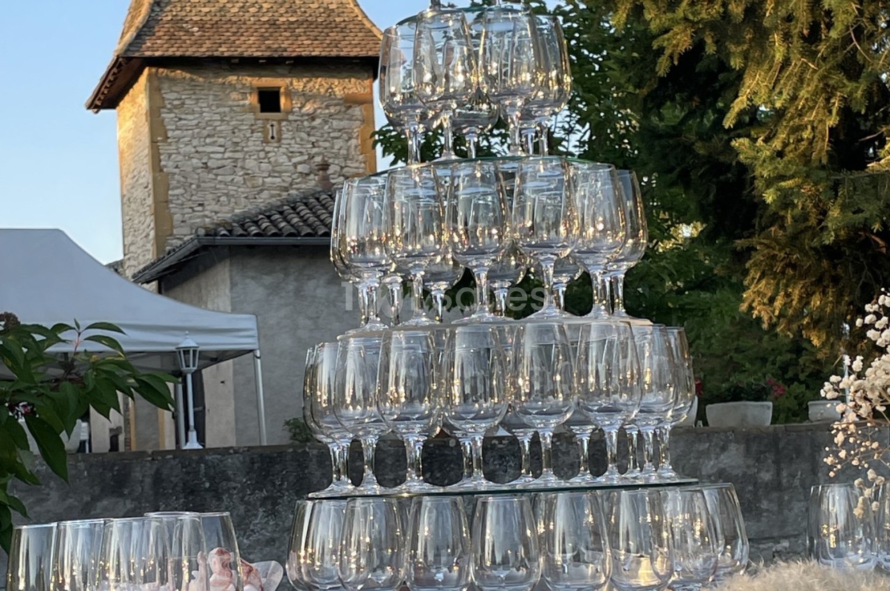 Tour de verres à pied empilés en pyramide, éclairés par la lumière naturelle, avec un bâtiment en pierre en arrière-plan.