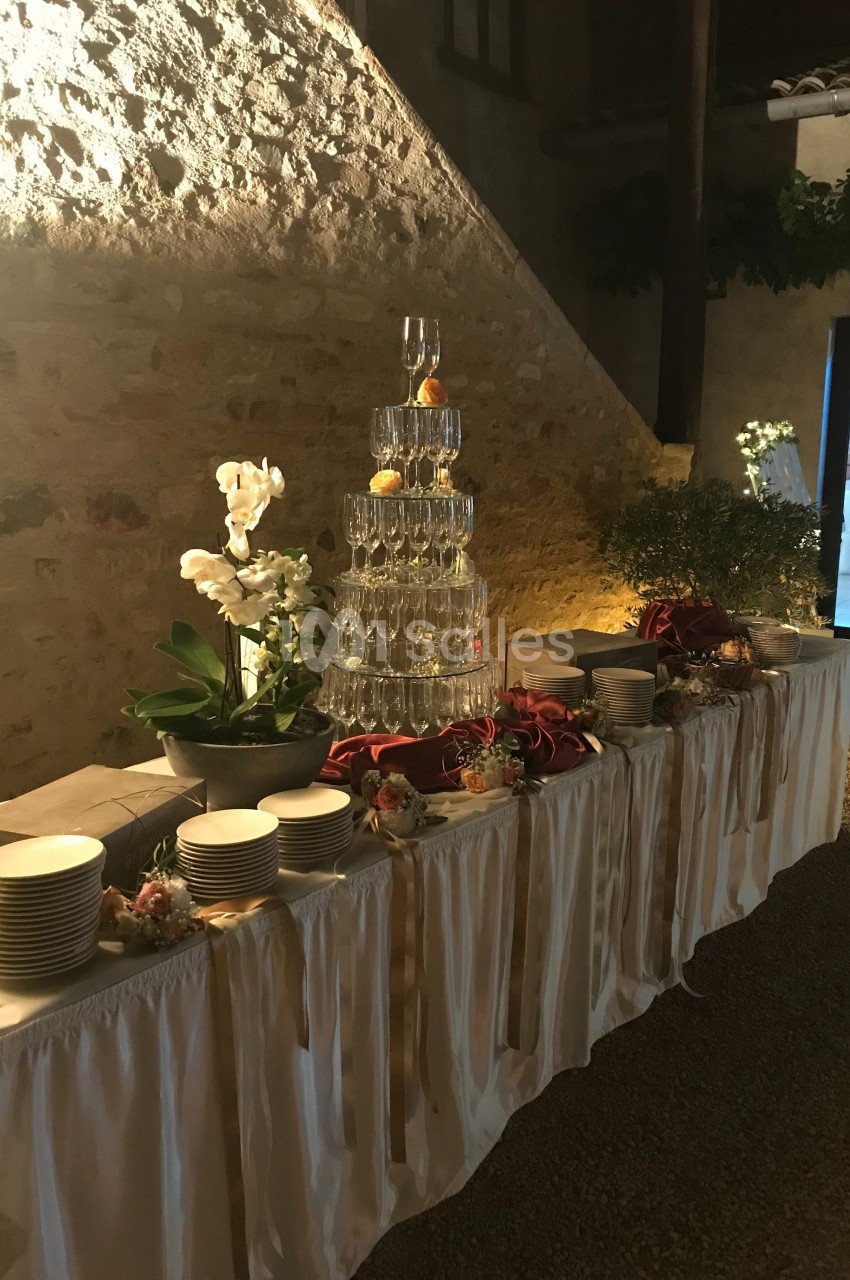 Table de réception décorée avec des assiettes, des fleurs, et une pyramide de verres surmontée de fruits.