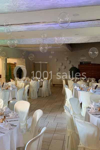 Salle de réception décorée avec des tables rondes dressées, chaises blanches et suspensions en forme de bulles.