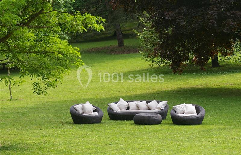 Mobilier de jardin en résine tressée avec coussins blancs disposé sur une pelouse entourée d'arbres.