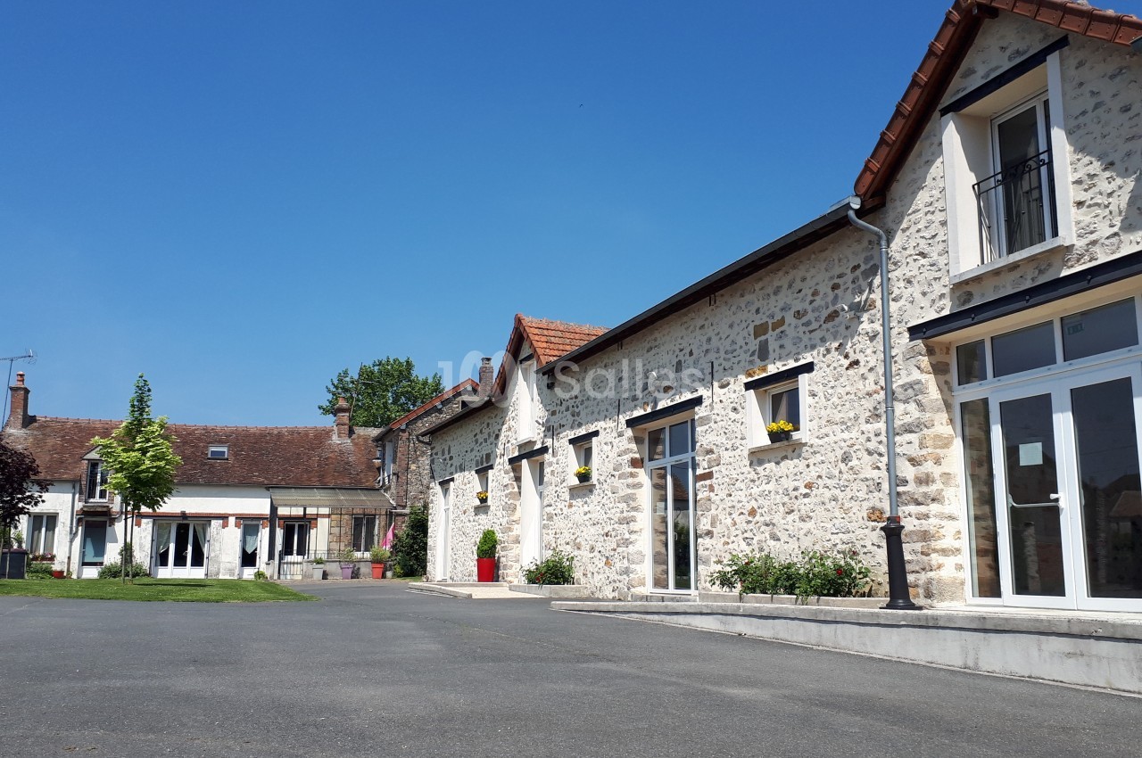 Bâtiments en pierre avec toits en tuiles rouges entourant une cour pavée sous un ciel bleu clair.