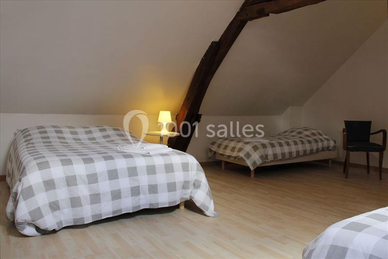 Chambre mansardée avec deux lits doubles à motifs carreaux, une lampe de chevet et une chaise en bois.