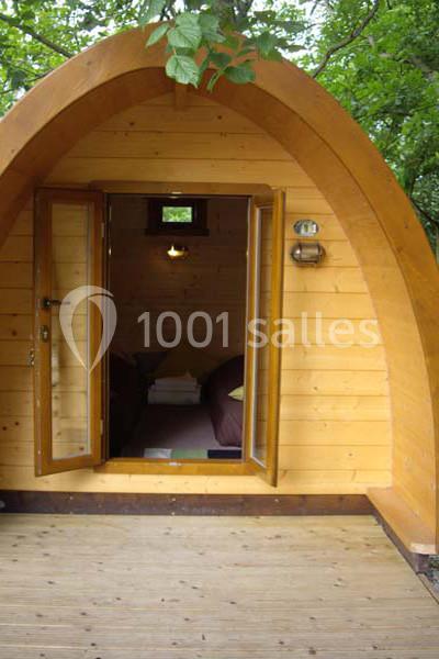 Cabane en bois en forme d'arche avec porte ouverte, révélant un intérieur aménagé sous un éclairage doux.