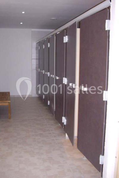 Rangée de cabines de toilettes avec portes en bois foncé, dans un espace carrelé et bien éclairé.