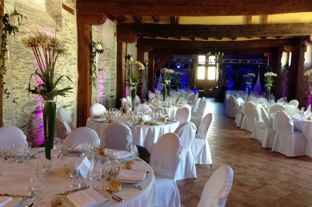 Salle de réception décorée avec des tables rondes dressées, nappes blanches et arrangements floraux.
