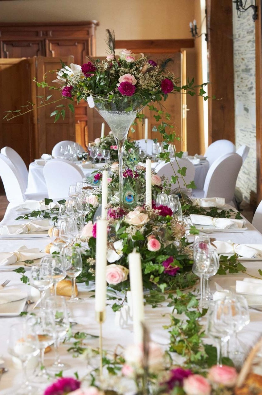 Table de réception décorée avec des fleurs roses et blanches, des chandeliers et des feuillages, dans une salle élégante.