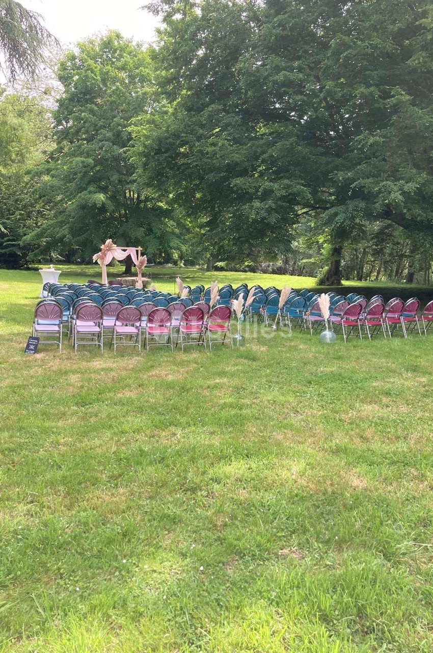 Chaises disposées en rangées sur une pelouse, face à une arche décorée, dans un cadre verdoyant en extérieur.