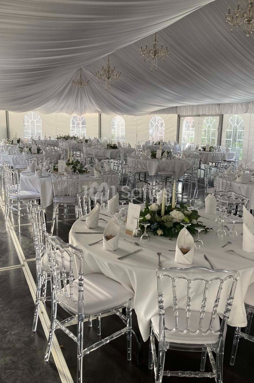 Salle de réception sous chapiteau avec tables rondes dressées, nappes blanches et décorations florales.