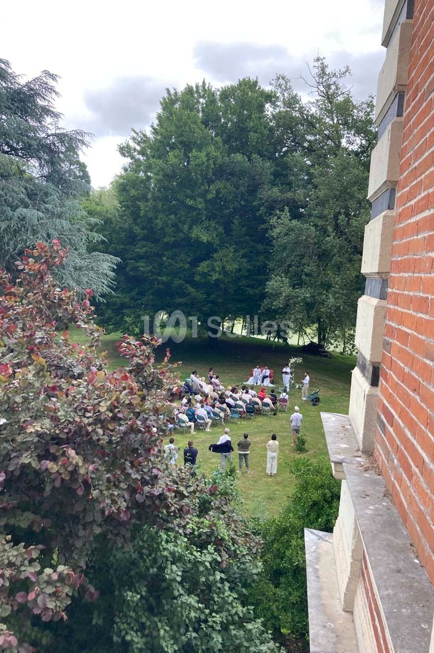 Groupe de personnes rassemblées dans un jardin verdoyant, vu depuis une fenêtre d'un bâtiment en briques.