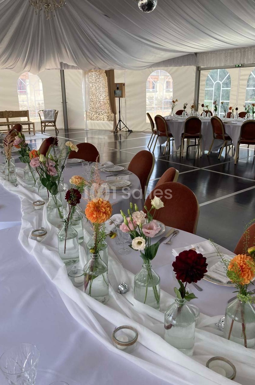 Salle de réception décorée avec des tables blanches ornées de fleurs colorées dans des vases en verre.